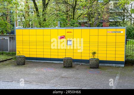 Hamburg, Deutschland - 05 04 2023: Blick auf eine gelbe DHL-Packstation am Rande eines Parkplatzes mit Bäumen im Hintergrund. Stockfoto