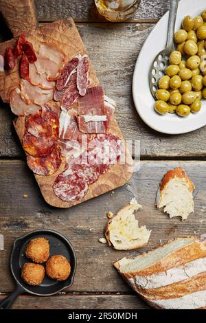 Eine Auswahl an gepökeltem Fleisch auf einem Holzbrett mit Brot und Oliven an der Seite Stockfoto