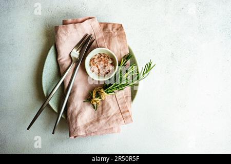 Minimalistisches Besteckset mit frischem Rosmarin und rosafarbenem himalaya-Salz auf Betontisch Stockfoto