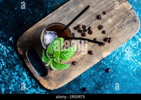 Schaumiiger Schlagkaffee White Russischer Cocktail im Glas serviert und mit Kaffeebohnen und frischen Minzblättern dekoriert Stockfoto