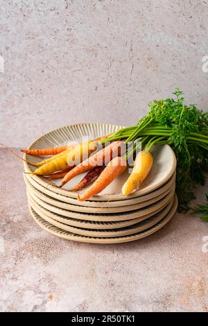 Ein Haufen bunter Bio-Karotten mit Grün auf einem Stapel handgefertigter Keramikplatten Stockfoto