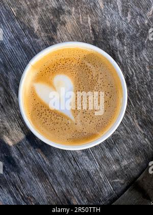 Flacher weißer Kaffee mit Herzdekoration in einem Pappbecher zum Mitnehmen Stockfoto