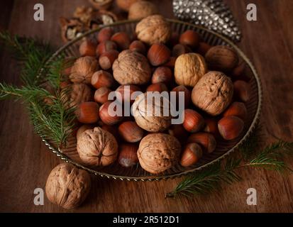 Haselnüsse und Walnüsse mit Zweigen von Piniennadeln in einer Silberschüssel Stockfoto