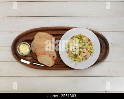 Penne mit Pesto und Garnelen serviert mit Brot und Butter auf einem Tablett Stockfoto