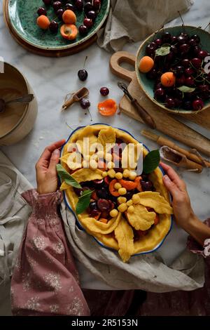 Torte mit Kirschen und Aprikosen. Eine Frau hält eine Fruchttorte in der Hand Stockfoto