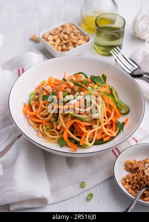 Lauwarmer Nudelsalat mit Gurke, Karotten, Erdnusscreme-Dressing und gerösteten Knödeln Stockfoto