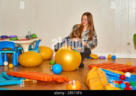 Hübsche Mutter spielt mit süßer Tochter Baby Mädchen im Spielzimmer im Kindergarten Stockfoto