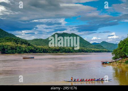 Ein traditionelles Laos-Slow-Boot gleitet durch das schlammige untere Becken des Mekong, umgeben von üppigem tropischem Dschungel und Ruhe nach Regen. Stockfoto