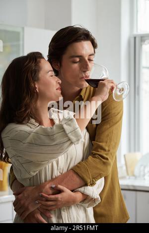 Junger Mann, der die Freundin umarmt und Wein aus ihrem Glas trinkt Stockfoto