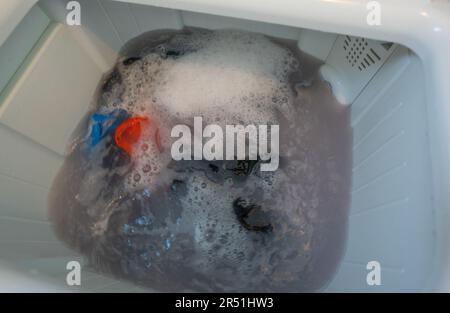 Schmutzige Kleidung in der Waschmaschine. Kleidung mit Waschmittelblase in der Waschmaschine. Wäschekonzept. Obere Lastscheibe. Hausarbeit Stockfoto