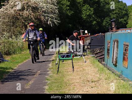 An einem warmen Frühlingstag findet ein Angelkampf statt, während Radfahrer auf einer Fahrt entlang des Leeds- und Liverpool-Kanals in Lancashire vorbeifahren. Stockfoto