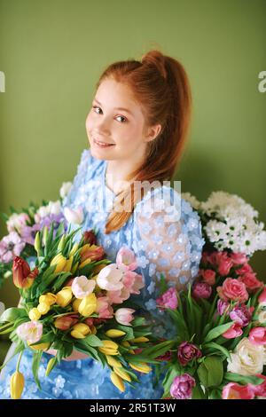 Porträt eines hübschen, jungen, 15 - 16 Jahre alten, rothaarigen Mädchens, umgeben von vielen Frühlingsblumen auf grünem Hintergrund, Schönheit und Modekonzept Stockfoto