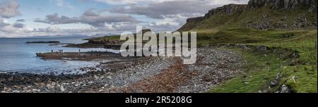 Panoramablick auf die felsige Küste, den Strand und das Gras am Ufer mit Gruppen von Menschen, die nach prähistorischen Dinosaurierspuren in den Felsen bei Ebbe suchen. Stockfoto