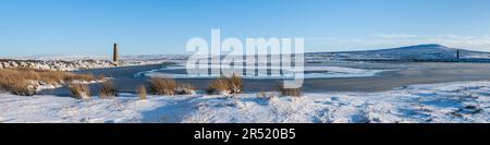 Sikehead-Staudamm, Reservoir und alte industrielle Schornsteine auf dem Grouse Moor der County Durham im Winter mit Gras, Schnee und Schatten der tiefen Sonne im Vordergrund Stockfoto