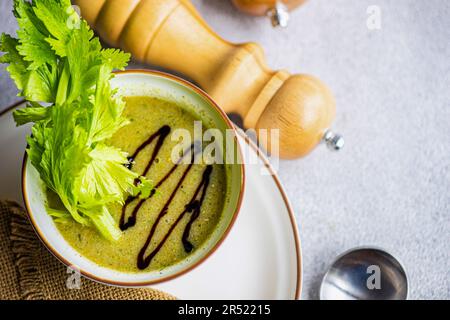 Draufsicht auf gesunde Selleriesahne Suppe in Schüssel mit Selleriestangen auf weißem Teller mit Serviette auf grauem Tisch mit Löffel und Salz und Pfeffer Holzgläser Stockfoto
