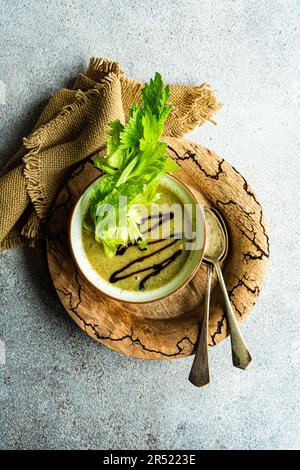 Draufsicht auf gesunde Selleriesahne Suppe in Schüssel mit Selleriestangen serviert auf Holzteller mit alten Löffeln auf grauem Tisch neben Serviette Stockfoto