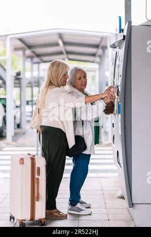 Ganzkörper-Seitenansicht von fokussierten älteren Reisenden mit Koffer, die Tickets im modernen Flughafenterminal kaufen, während sie auf den Flug warten Stockfoto