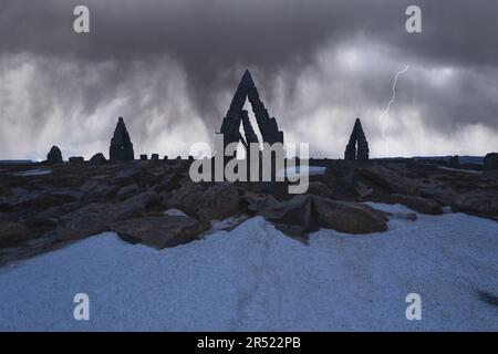 Von unten aus der Silhouette von Stein Henge Kreis von gestapelten Felsen auf einem felsigen Hügel vor bewölktem Himmel mit Blitzen im Winter Stockfoto