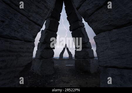 Silhouette des Henge-Kreises mit alten Steinsäulen und bogenförmigen Passagen an bewölkten Tagen mit Blitzhimmel über sandigem Boden Stockfoto