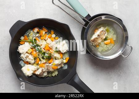 Draufsicht von Bratpfannen mit Gemüse und Fisch in Erdnussöl und Kräutern in Fumet mit Karotten und trockenem Fisch auf grauer Oberfläche in der Küche Stockfoto