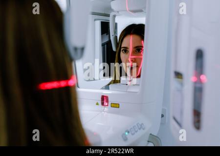 Junge Frau in legerer Kleidung im Stehen und mit Dentalröntgen-Digitalscanner-Panoramamaschine in einer hellen Klinik Stockfoto