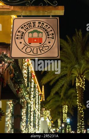 St. Augustine, Florida - 30. Dezember 2022: Schild für den Stand der Old Town Trolley Tours, während der Nacht der Lichter. Weihnachtslichter Bokeh im Hintergrund Stockfoto