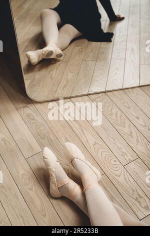 Großer Winkel einer nicht erkennbaren Balletttänzerin, die auf dem Boden in pointe-Schuhen vor dem Spiegel sitzt, während sie sich während der Probe im Studio ausruht Stockfoto