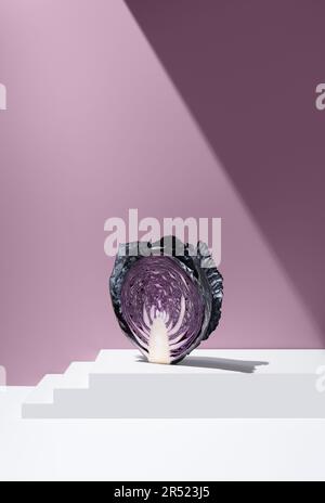 Querschnitt des in Scheiben geschnittenen Purpurkohls auf einer weißen, gestuften, Ebenen Oberfläche vor violettem Hintergrund im Studio Stockfoto