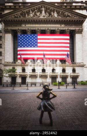 Wall Street Fearless Girl - die New Yorker Börse mit der großen amerikanischen Flagge und dem Fearless Statue Girl im Vordergrund. Dieses Bild ist al Stockfoto