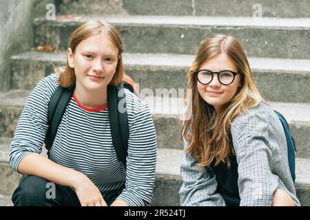 Außenporträt von zwei Teenagern, die auf der Treppe sitzen, den Rücken tragen und in die Kamera schauen Stockfoto