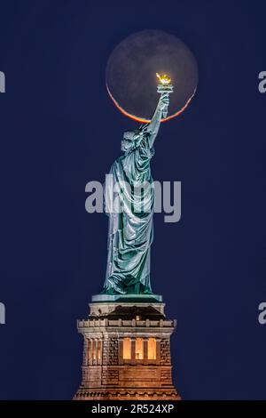 Lady and the Moon - die berühmte und historische Freiheitsstatue im Hafen von New York mit dem Halbmond hinter ihrem Arm, der die Fackel hält. Stockfoto