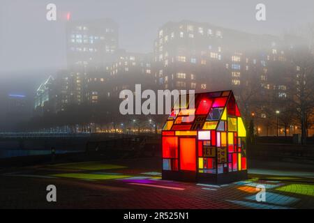 Farbenfrohes Glashaus - die beleuchtete Skulptur des Taxicab-Glashauses aus dem Jahr Hi5 von Tom Fruin. Der starke Nebel am Hudson River bedeckt die Skyline von Hoboken und Stockfoto