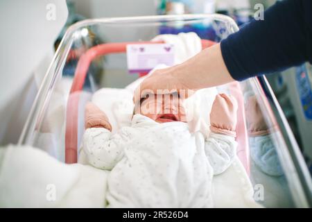 Weinendes Neugeborenes Baby im Krankenhausbett, Vater versucht, das Kind zu beruhigen, indem er seine Hand oh ihren Kopf legt Stockfoto