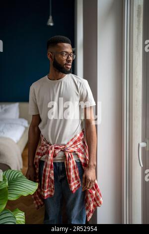 Einheimisches Porträt eines bärtigen afroamerikanischen Typen in lässiger Kleidung, der in einer modernen Wohnung steht Stockfoto