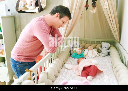 Vater bewundert, wie ein Neugeborenes in einem Kinderbett schläft, die ersten Tage seines Lebens Stockfoto