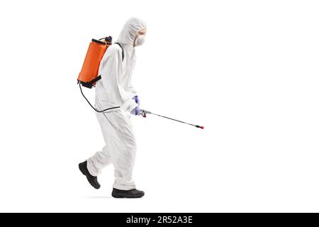 Profilaufnahme eines Berufstätigen in einem Schutzanzug beim Gehen und Sprühen eines Desinfektionsmittels isoliert auf weißem Hintergrund Stockfoto