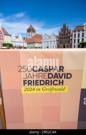 31. Mai 2023, Mecklenburg-Vorpommern, Greifswald: Ein Aussteller mit der Inschrift "250 Jahre Caspar David Friedrich 2024 in Greifswald" steht auf dem Markt. Neben einem umfangreichen Kulturprogramm wird der 250. Geburtstag des Malers Caspar David Friedrich im kommenden Jahr auch bleibende Spuren in seiner Heimatstadt Greifswald hinterlassen. Die neuen Ostfenster in der Kathedrale sollen im April eröffnet werden. Nach Angaben der Stadt soll das Jubiläumsjahr in der Kathedrale feierlich am 20. Januar 2024 eröffnet werden. 160 Ereignisse wurden bereits bereut Stockfoto