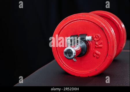 Kurzhantel mit roten Gewichten auf einer schwarzen Trainingsbank für Krafttraining, einsatzbereit auf schwarzem Hintergrund Stockfoto