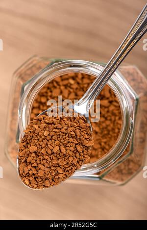Instant-Granulatkaffee in einem Löffel über einem Glas auf Holzhintergrund. Speicherplatz kopieren. Stockfoto