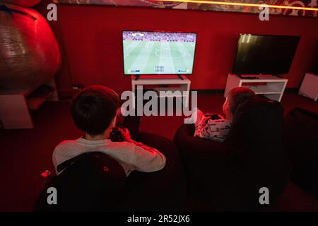 Zwei Jungen spielen die Videospielkonsole des Football-Gamepads im roten Spielzimmer. Stockfoto