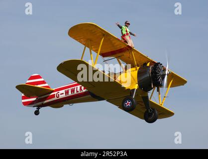 Ein Boeing A-75L300 Stearman Doppeldecker der Wing Walk Company in Aktion mit Wing Walkern am Headcorn Aerodrome Kent England Stockfoto