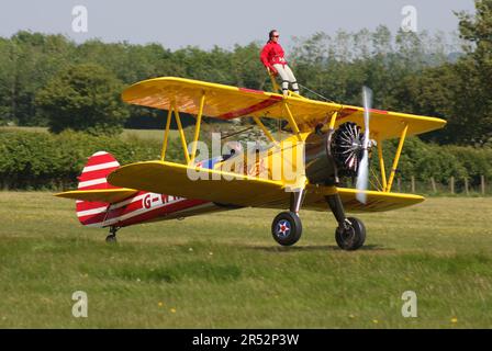 Ein Boeing A-75L300 Stearman Doppeldecker der Wing Walk Company in Aktion mit Wing Walkern am Headcorn Aerodrome Kent England Stockfoto