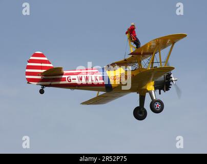 Ein Boeing A-75L300 Stearman Doppeldecker der Wing Walk Company in Aktion mit Wing Walkern am Headcorn Aerodrome Kent England Stockfoto