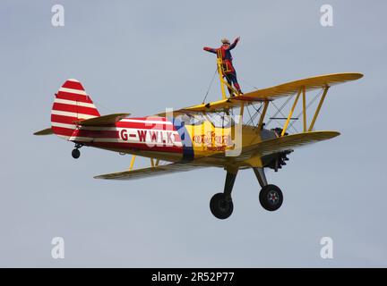 Ein Boeing A-75L300 Stearman Doppeldecker der Wing Walk Company in Aktion mit Wing Walkern am Headcorn Aerodrome Kent England Stockfoto