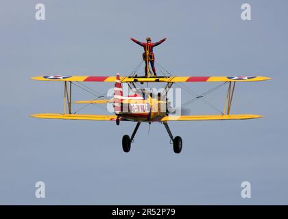 Ein Boeing A-75L300 Stearman Doppeldecker der Wing Walk Company in Aktion mit Wing Walkern am Headcorn Aerodrome Kent England Stockfoto