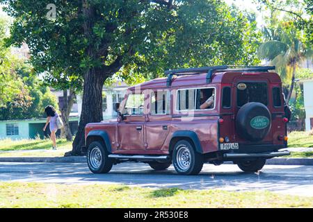 Ein rotes, altes kubanisches Auto fährt auf einer Straße in Havanna, Kuba, mit einem Land Rover Reifen auf der Rückseite des Fahrzeugs. Stockfoto