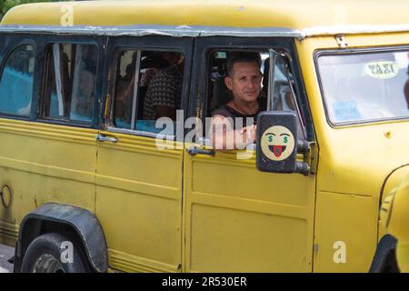 Der Passagier in einem kubanischen Taxi schaut aus dem Fenster und lächelt, während das Taxi die Straße in Havanna, Kuba, hinunter fährt. Stockfoto