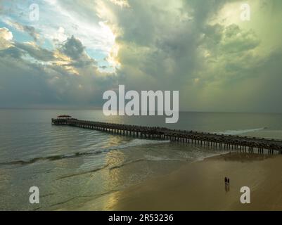 Aus der Vogelperspektive die Brücke erstreckt sich bei schönem Sonnenuntergang bis ins Meer. Atemberaubende Wolken, die sich am blauen Himmel bewegen. Wunderschöne Sonnenuntergangslandschaft, herrliches Licht der Natur Stockfoto