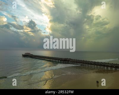 Aus der Vogelperspektive die Brücke erstreckt sich bei schönem Sonnenuntergang bis ins Meer. Atemberaubende Wolken, die sich am blauen Himmel bewegen. Wunderschöne Sonnenuntergangslandschaft, herrliches Licht der Natur Stockfoto