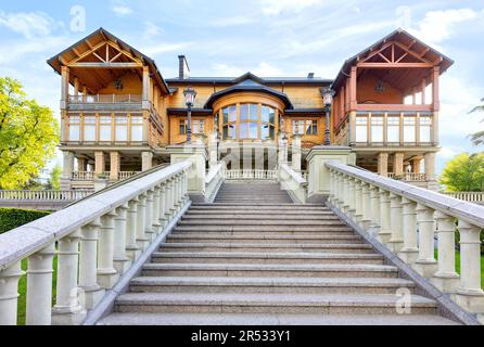 Eine stilvolle Granittreppe mit einer Balustrade mit wunderschön geschnitzten Balustern führt zur Fassade eines wunderschönen Holzhauses. Stockfoto